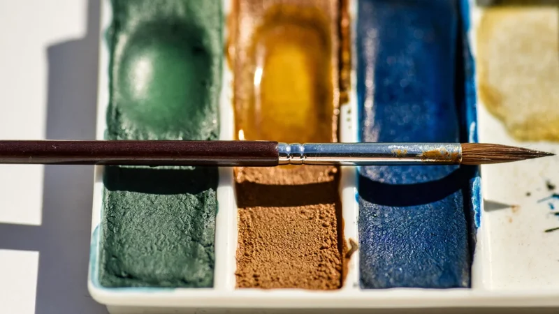 Aquarellnäpfchen in erdigen und blauen Tönen mit feuchtem Pinsel, illustrative Darstellung